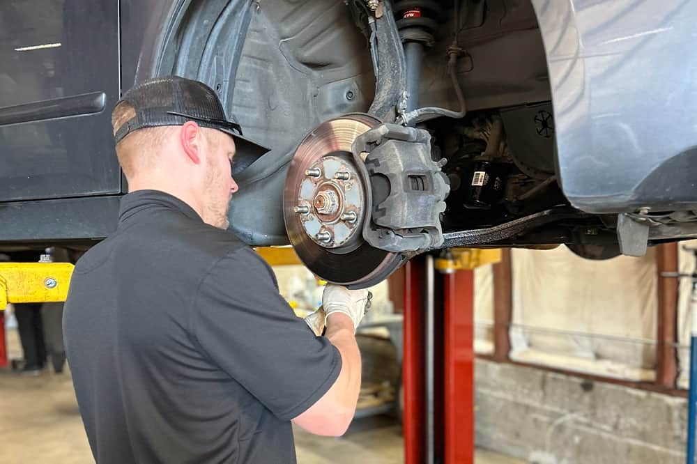 Brake repair and services near me in Colorado Springs, CO with Legend Motor Works. Image of a mechanic inspecting the brake pads and brake rotor of a car being lifted as part of brake inspection and repair services.
