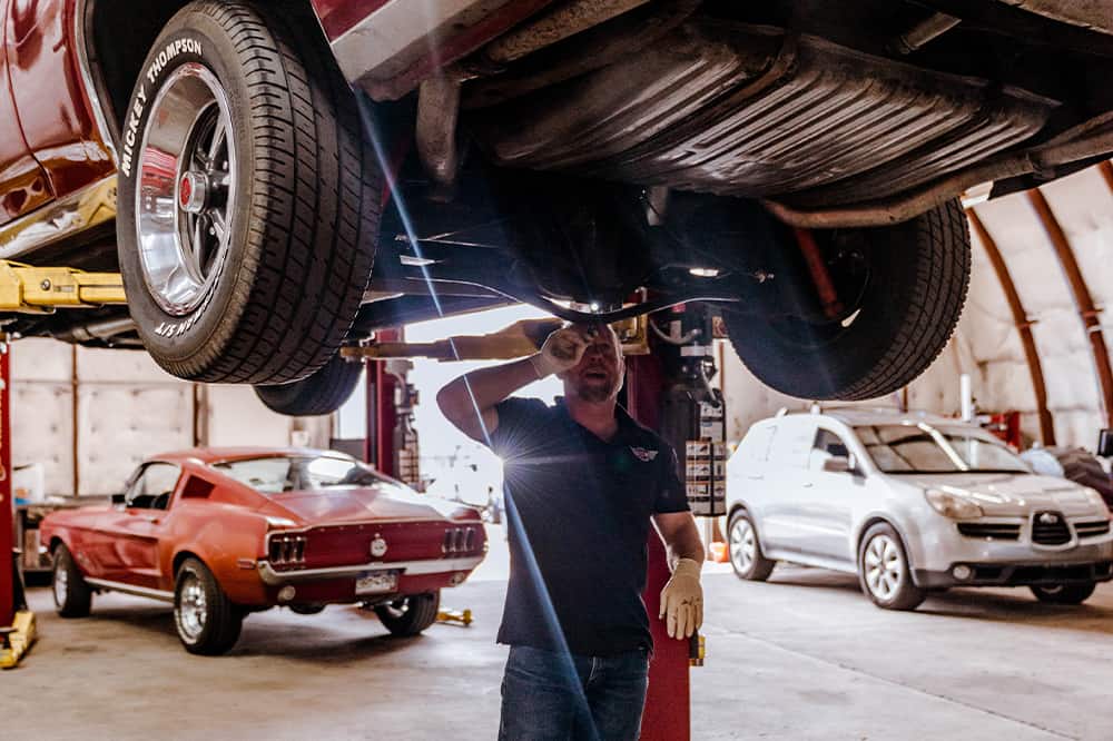Steering and Suspension Repair Services near me in Colorado Springs, CO with Legend Motor Works. Image of a mechanic checking the suspension system of a car being lifted for steering and suspension repair.