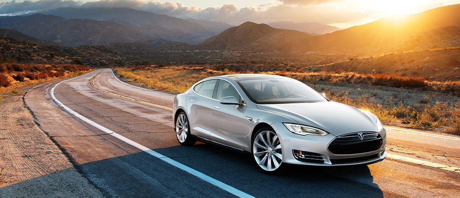 Tesla Repair and Service near me in Colorado Springs, CO with Legend Motor Works. Image of grey Tesla model S driving on the road with the sun setting in the background in colorado.