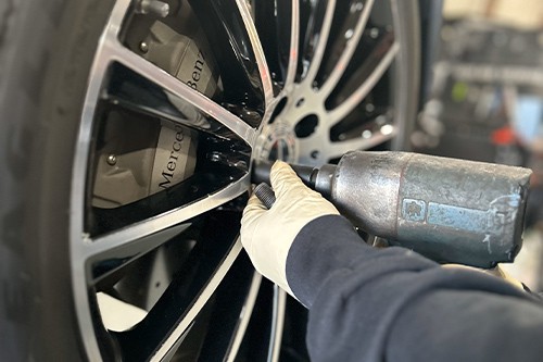 Wheel alignment in Colorado Springs, CO at Legend Motor Works. Image of mechanic hand using tool to take lug nuts off of a tire that came in for wheel vibration issues.